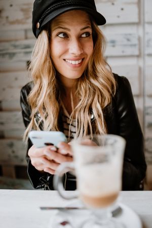 Smiling curly woman browsing smartphone at table