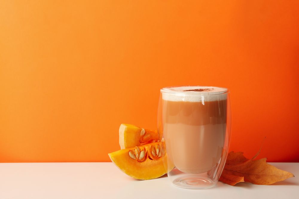 Glass of pumpkin latte, leaf and pumpkin on orange background