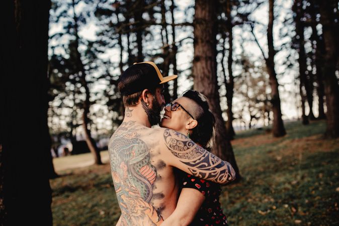 Young guy in tattoos hugging woman in forest