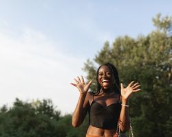A young Black woman, with braids in her hair, gesticulates and gets excited, during a walk in the park at sunset