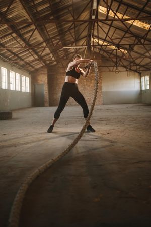 Female working out with battle rope at gym inside old warehouse