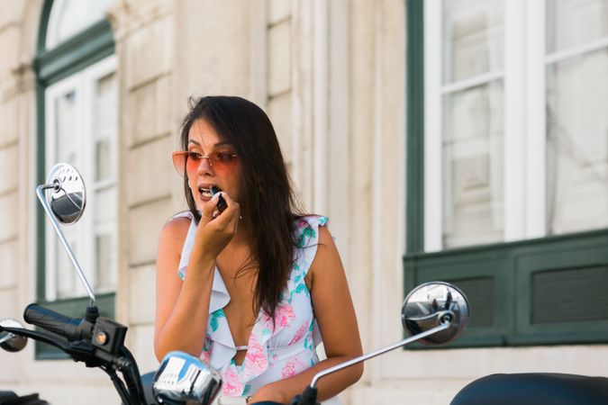 Woman putting lipstick looking at motorcycle mirror