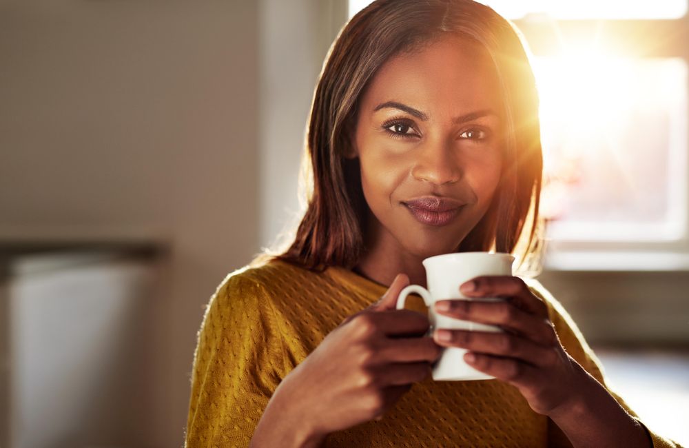 Portrait of Black woman with coffee in sunny room