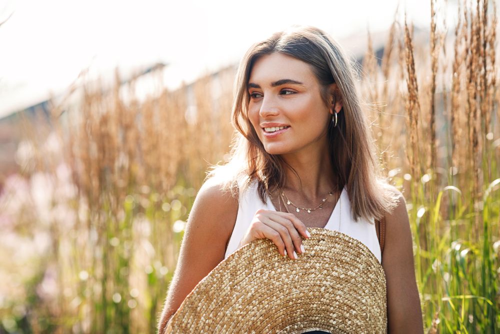 Woman in beige top holding a straw hat on sunny day