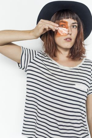 Female in striped shirt and felt hat holding transparent orange material to eye, vertical