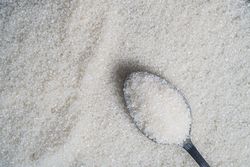 Granulated sugar spread on a surface with a spoonful resting on top
