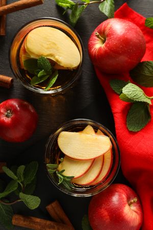 Glasses with apple cider, mint leaves and red apples on dark wooden background, top view
