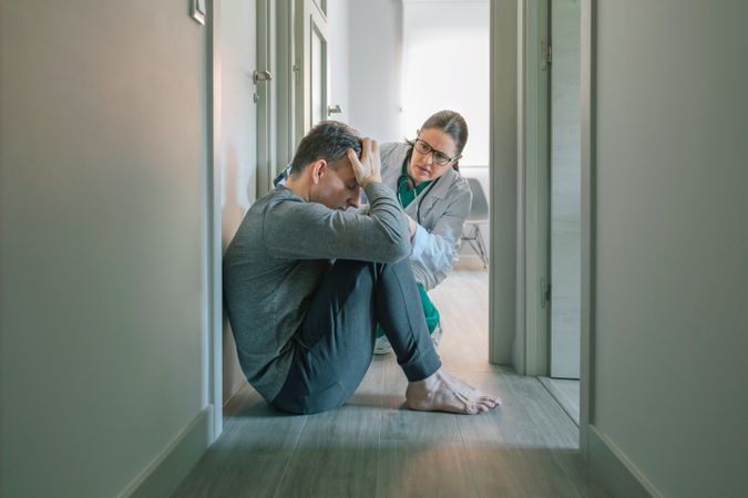 Psychiatrist reassuring and helping to patient sitting on room floor