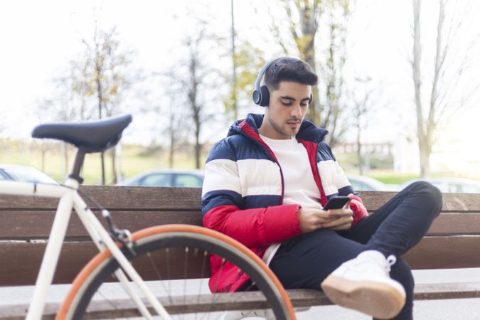Man relaxing with bicycle checking smartphone while sitting on bench