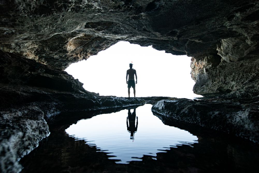 Silhouette of man standing beside river and cave