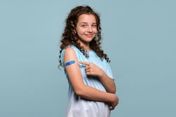 Smiling girl pointing at bandage on vaccinated arm.
