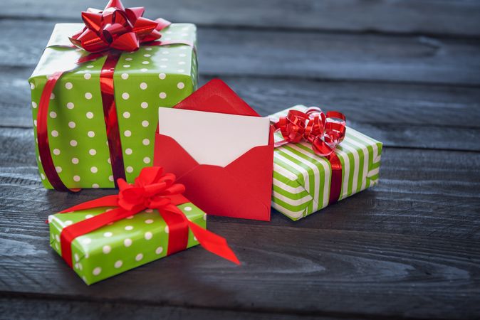 Three gifts wrapped in green paper with bows on wooden table