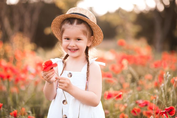 Girl holding red poppy flower in meadow outdoor