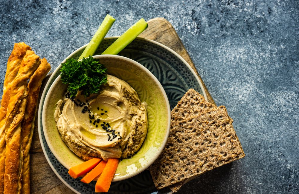 Top view of creamy hummus and chopped vegetables on grey kitchen counter with space for text