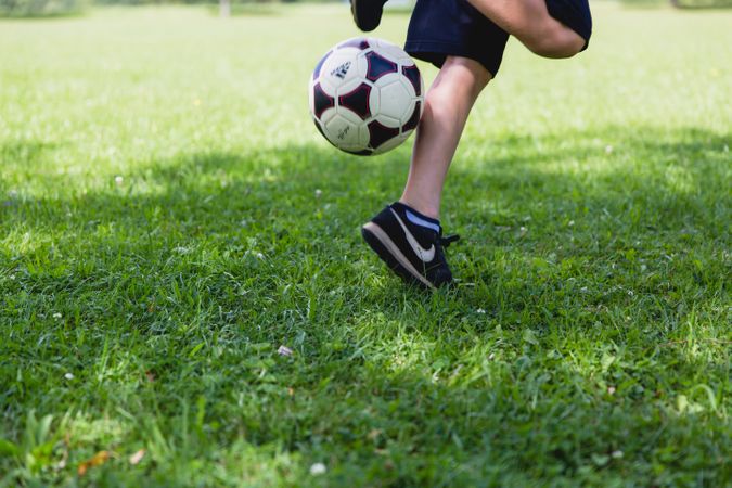 Cropped image of boy playing soccer ball on green grass field