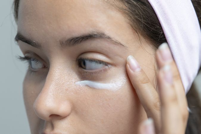 Woman applying under-eye cream for dark circles, a close-up on skincare beauty treatment.