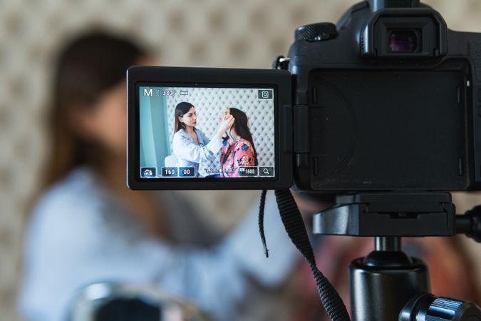 Cheerful visagiste applying makeup on model and recording video