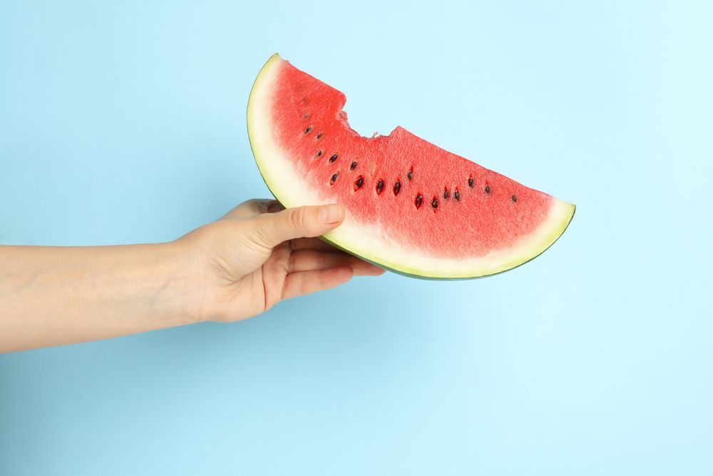 Female hand holds watermelon slice on blue background. Summer fruit
