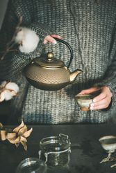 Woman in cozy sweater pouring from traditional Japanese tea set, with dried cotton