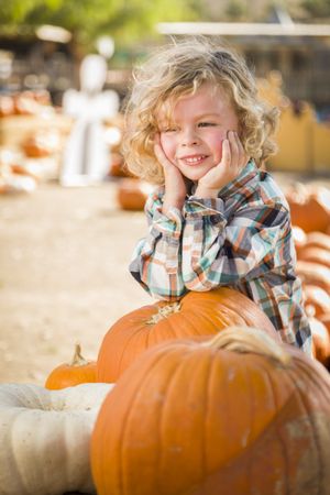 Boy Smiles While Leaning on Pumpkin at Pumpkin Patch