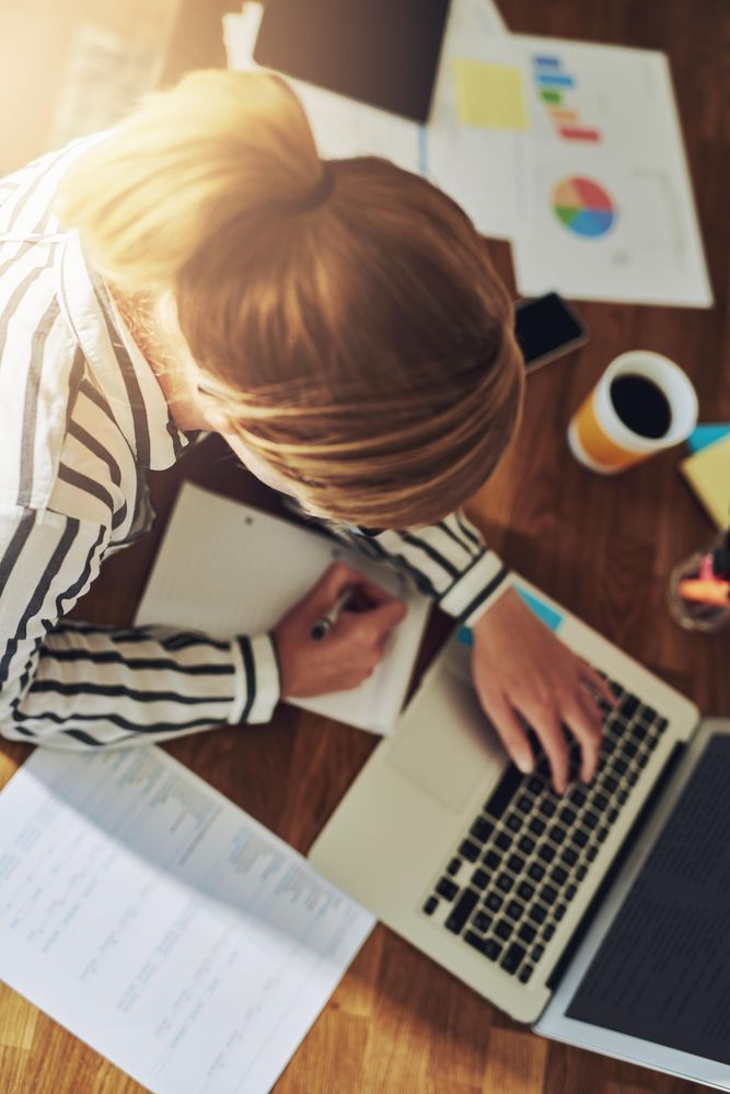 Looking down at woman in striped shirt working on laptop, vertical
