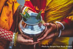 Cropped image of Indian women wearing saris holding a metal jar with herbs 0WLKM5