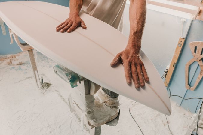 Man holding surf board on stand in workshop