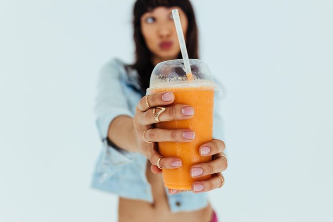 Close up of female hands holding fresh orange juice glass in front