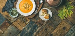 Pumpkin soup with croutons, bread, seeds, pot, spoon on wooden table, wide composition, copy space