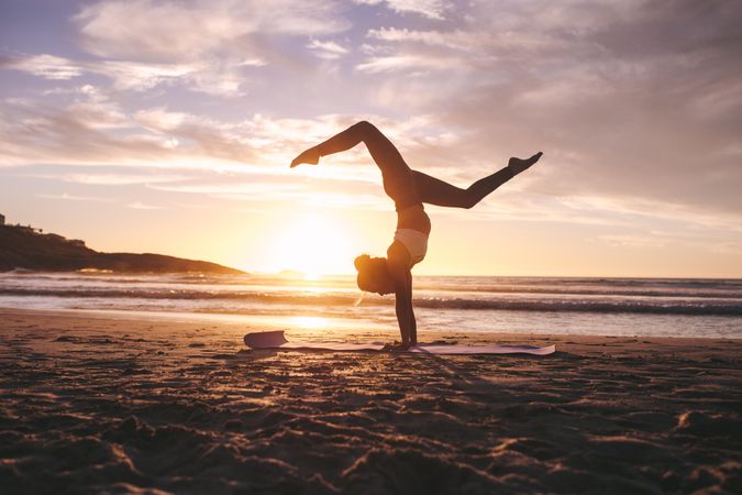 Flexible female exercising on yoga mat at sunset