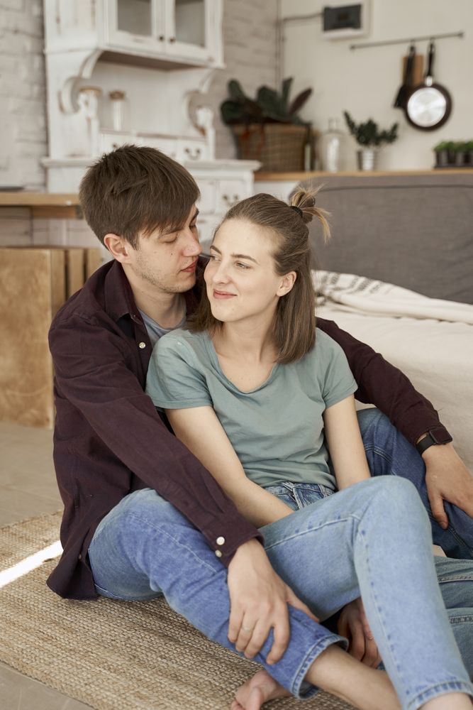 Relaxed couple hugging while sitting together on floor in living room