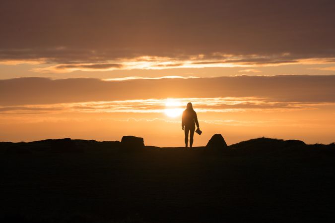 Woman with book standing at sunset