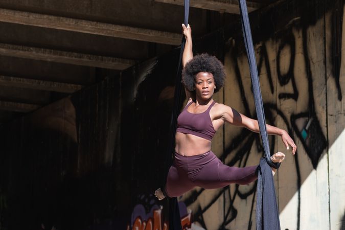 Slim woman doing yoga with aerial silks in city
