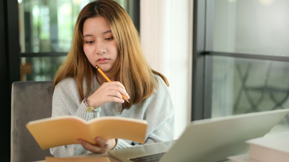 Woman holding pencil and notebook serious gesture with laptop on desk,online learning,work at home.