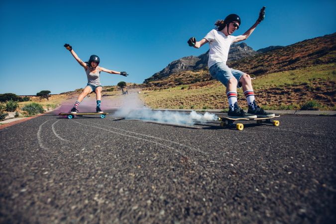 Full length shot of young man and woman outdoors longboarding down the road