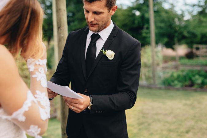 Handsome young groom reading wedding vows from a paper