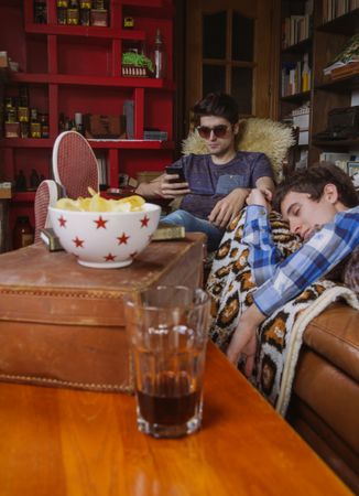 Young man sleeping on sofa and friend looking smartphone