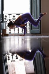 Fit woman doing Eka Pada Koundinyasana yoga pose on mat at home