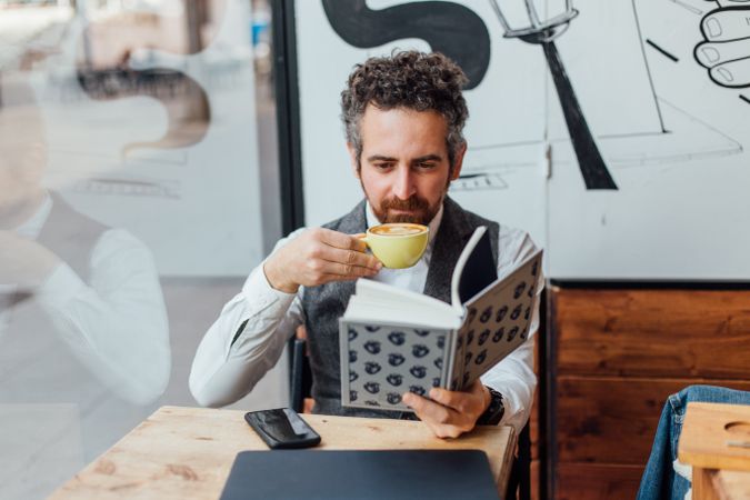 Man sipping coffee in trendy cafe with book