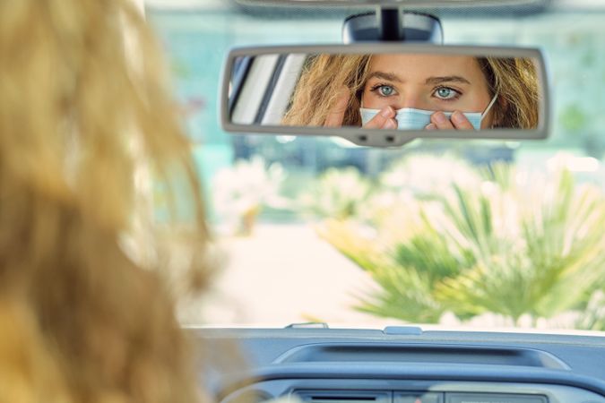 Crop woman putting on face mask against auto mirror