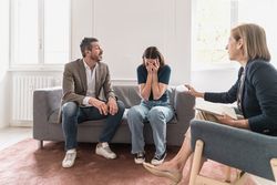 A woman cries covering her face with her hands during a therapy session