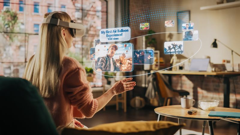 Woman Sitting in Loft Living Room at Home, Using Virtual Reality Headset with Controllers to Check Social Media Streaming App