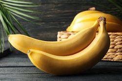Banana cluster and basket with bananas on wooden background