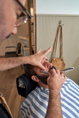 Professional barber trimming beard of client