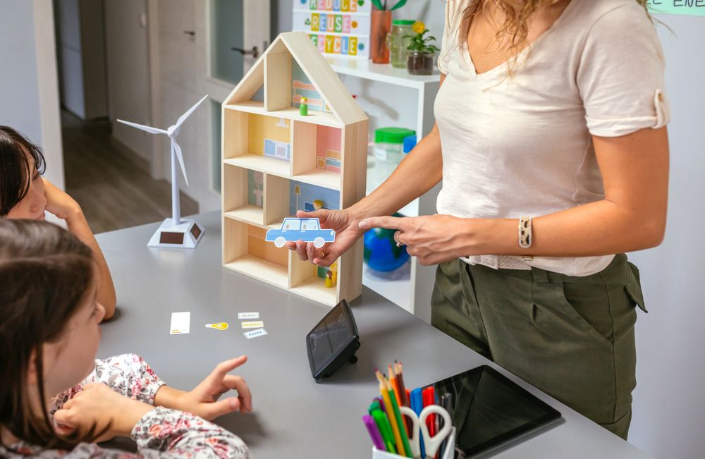 Teacher explaining to her students the parts of a sustainable house showing an electric car