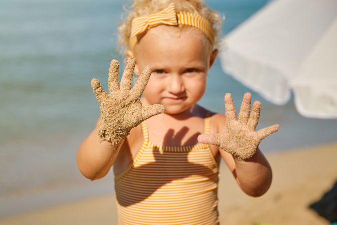 Girl demonstrating sandy hands on seashore