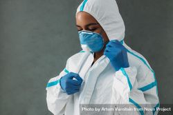 Black woman adjusting her hazmat suit in protective gloves and face mask 0yArO0