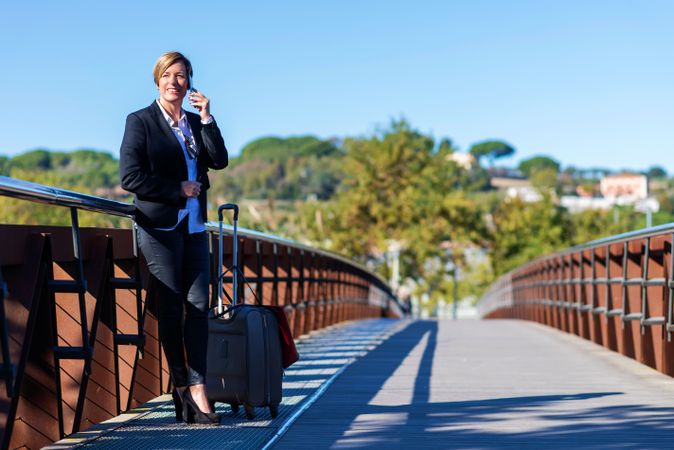 Traveling business woman standing on pedestrian bridge speaking on cell phone