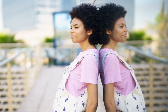 Bemused female in floral overalls leaning back on window outside