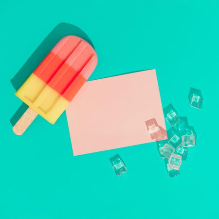 Ice cream popsicle with ice cubes and pink paper card note on vivid blue background